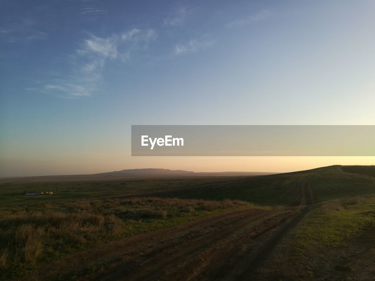 Dirt road amidst field against sky during sunset