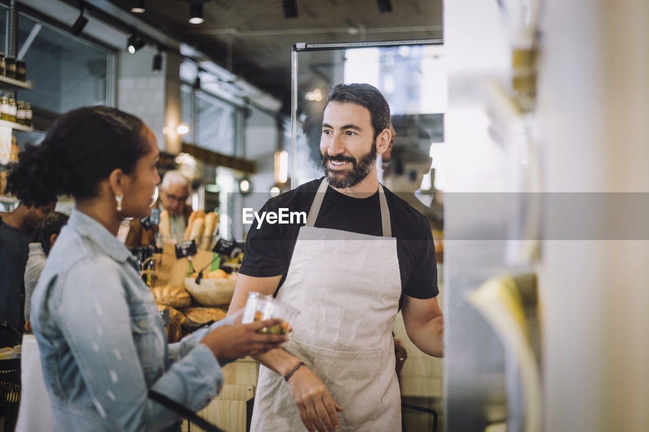 Smiling mature salesman discussing over product with female customer at delicatessen