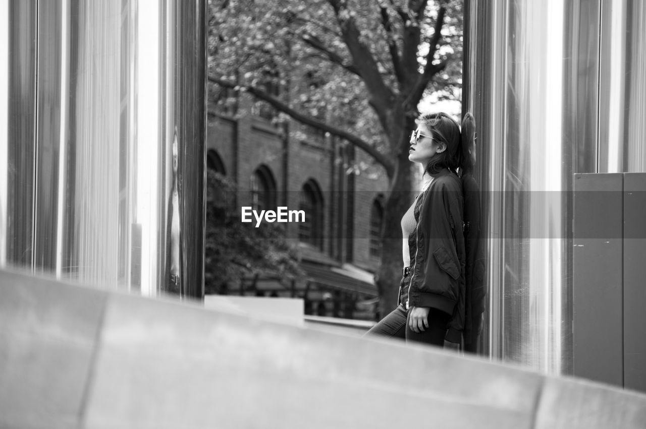 Side view of young woman standing by metal column in city