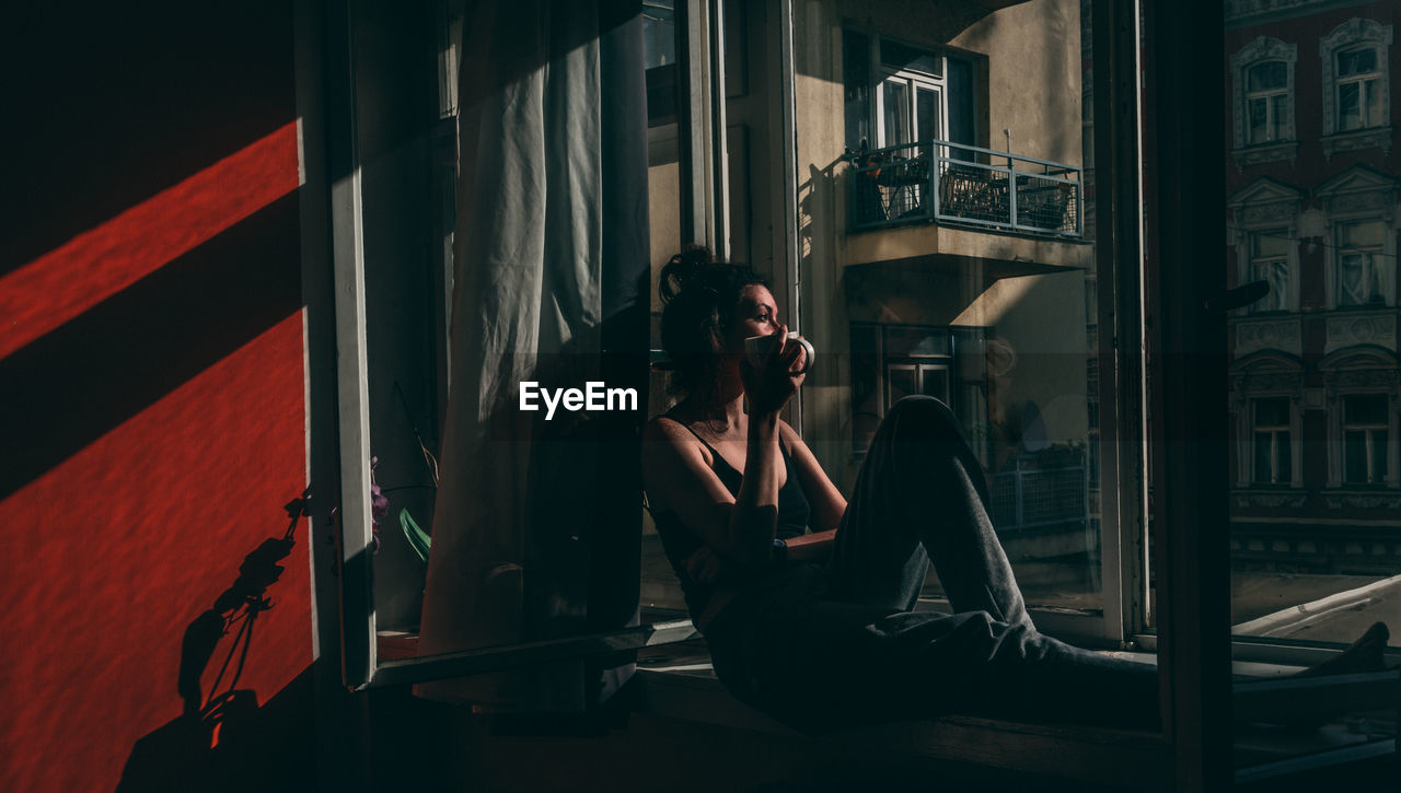 Full length of woman sitting by window in darkroom