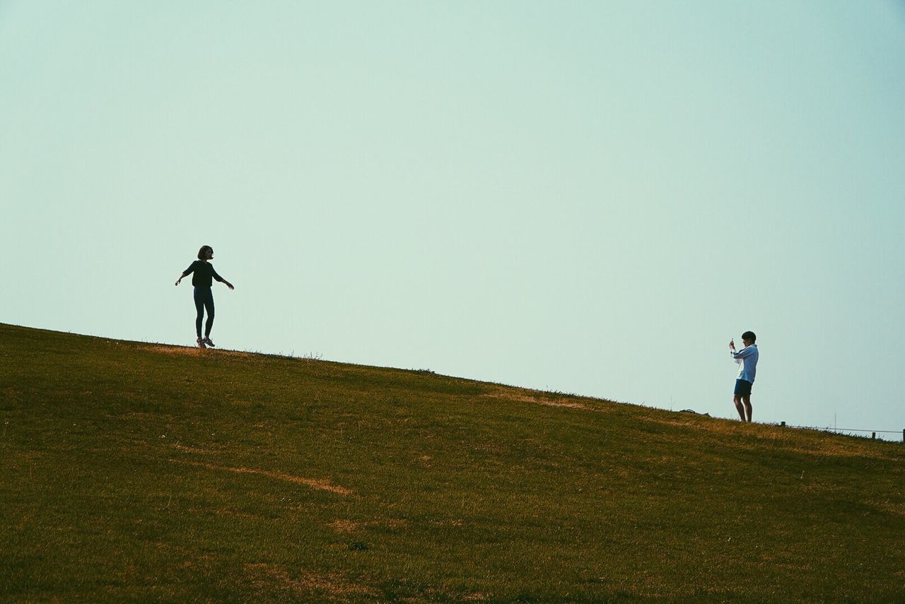Man and woman standing on grassy hill against clear sky