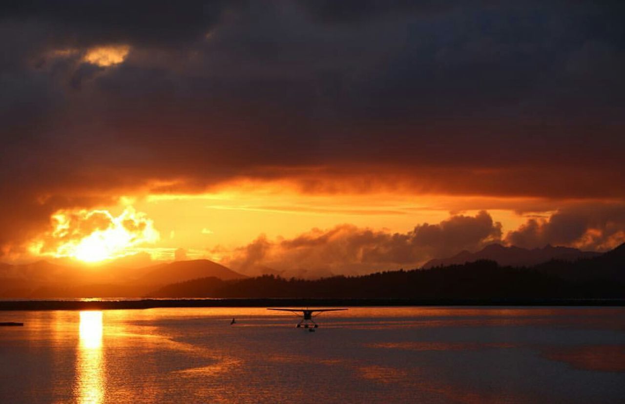 Silhouette seaplane on sea against cloudy sky during sunset