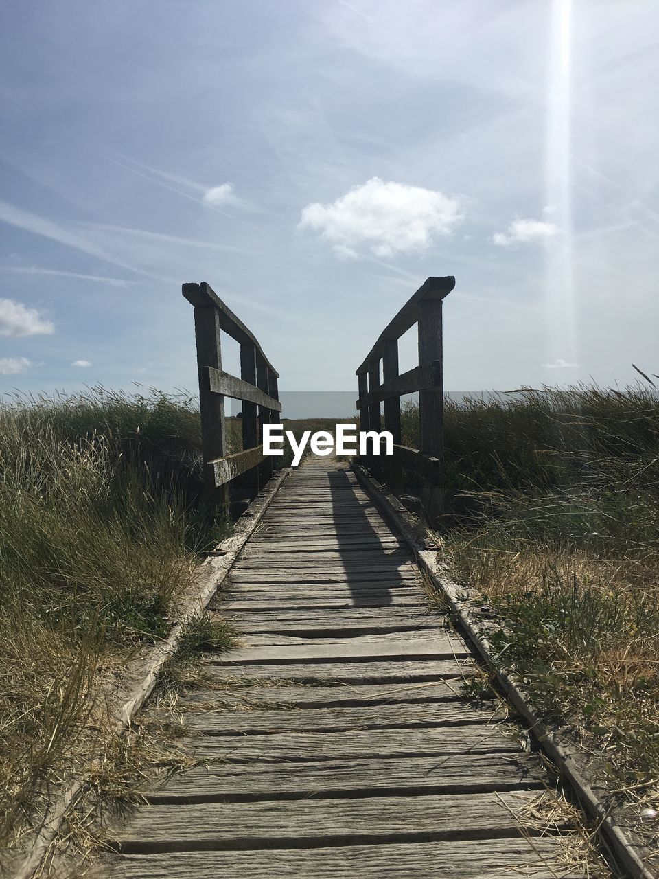 Boardwalk leading towards built structure against sky