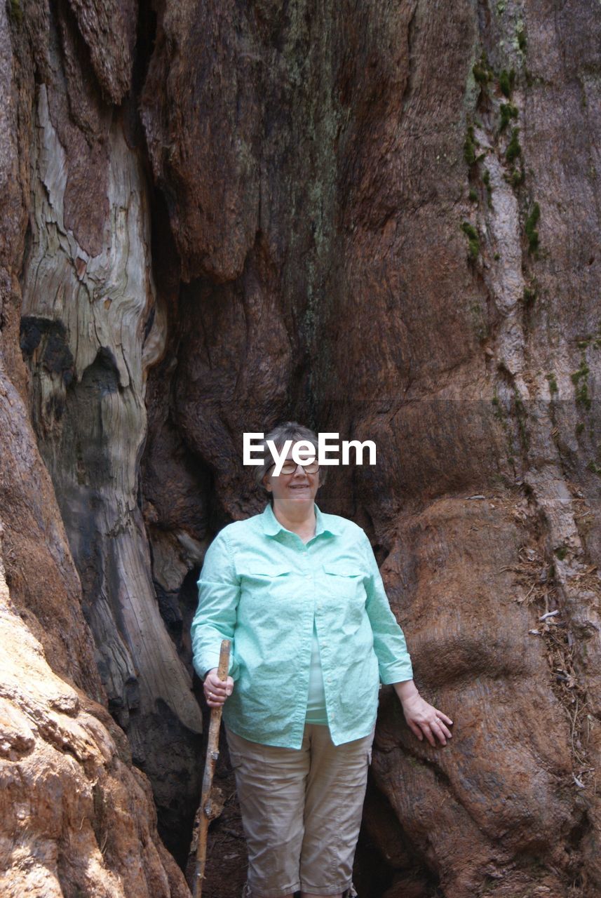 Smiling senior woman standing against sequoia tree trunk