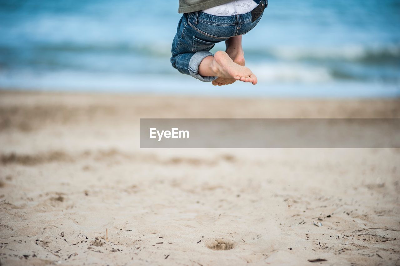 Low section of boy jumping on sand at beach