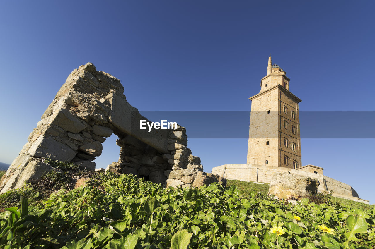 Tower of hercules on field against clear blue sky