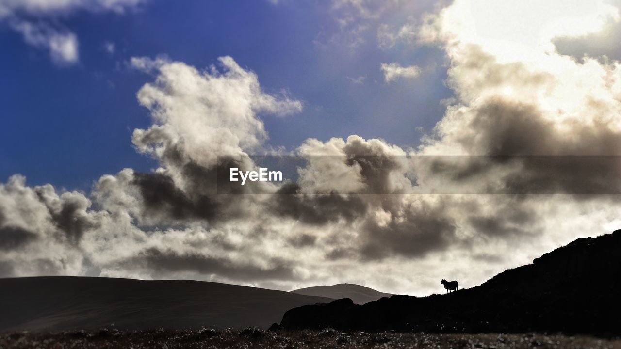 LOW ANGLE VIEW OF CLOUDS OVER SILHOUETTE MOUNTAINS