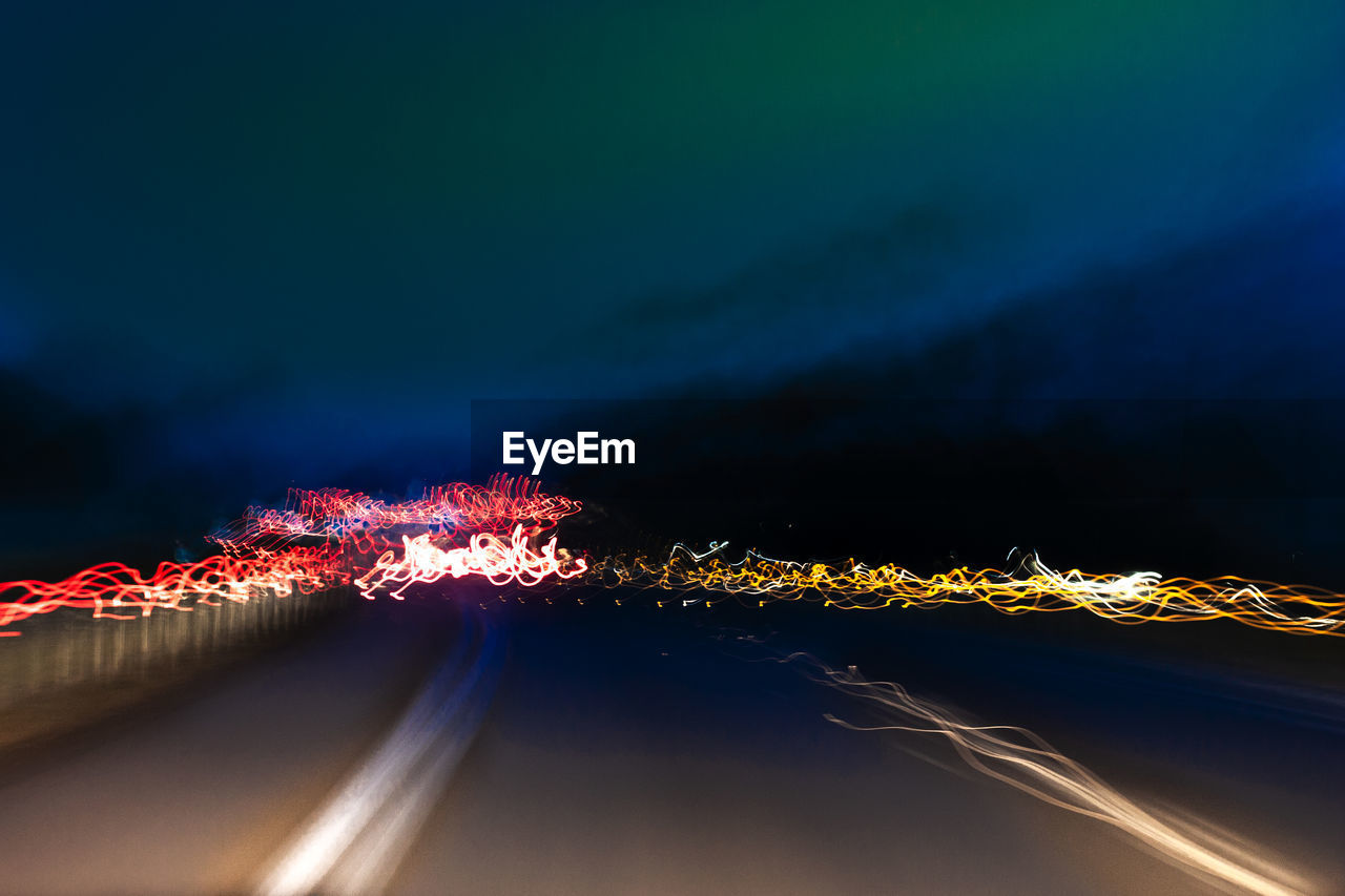 Light trails on road by illuminated city against sky at night