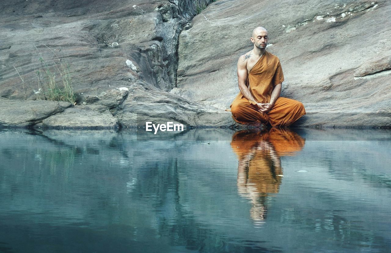 Reflection of monk meditating on lake