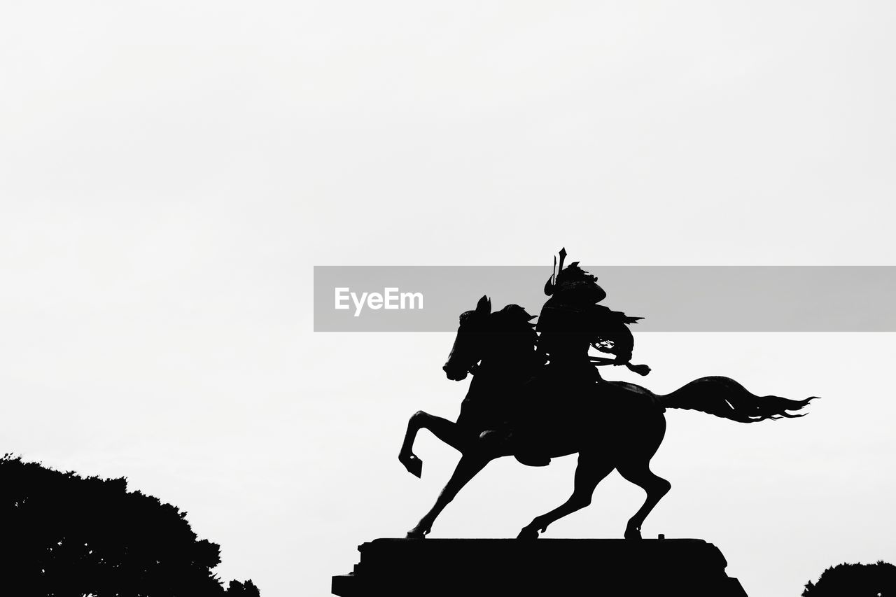 LOW ANGLE VIEW OF SILHOUETTE MAN RIDING STATUE AGAINST SKY