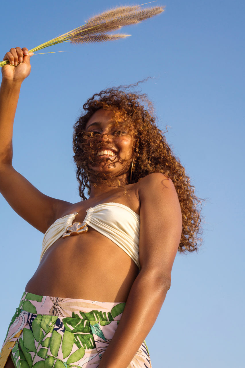 Low angle portrait of young woman with dark skin and long curly hair at the beach