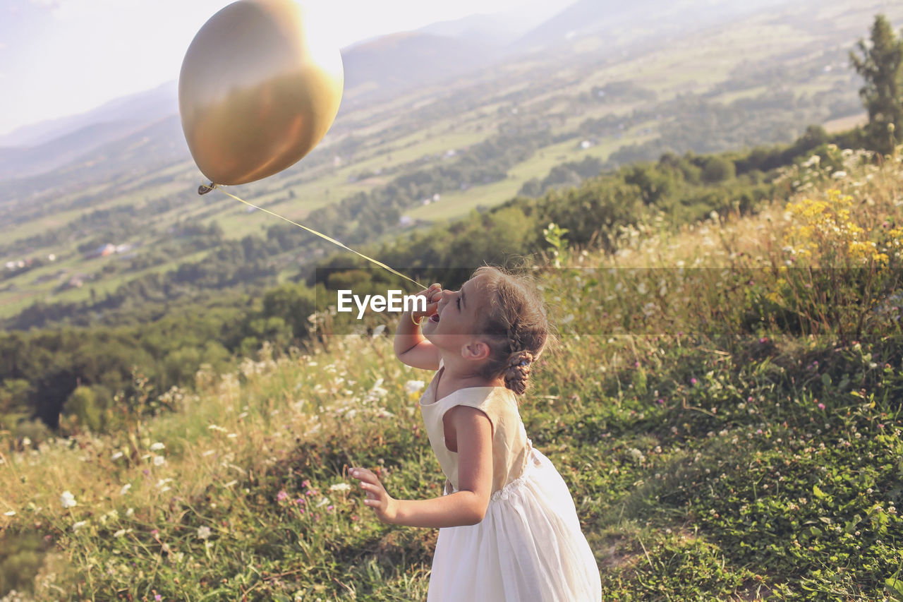 Side view of girl holding balloons on field