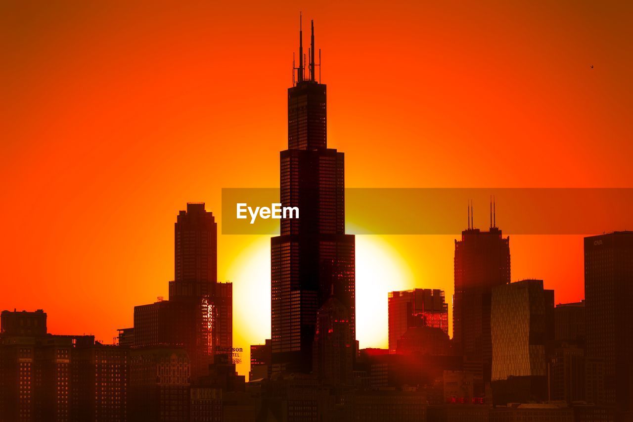 Silhouette buildings against orange sky during sunset