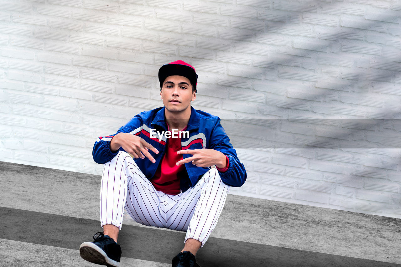 A teenage boy agains white brick wall. a male teenager model wearing casual clothing. 