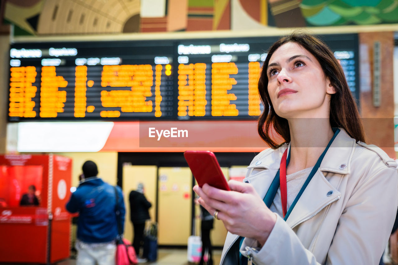 Young businesswoman holding smart phone while looking up