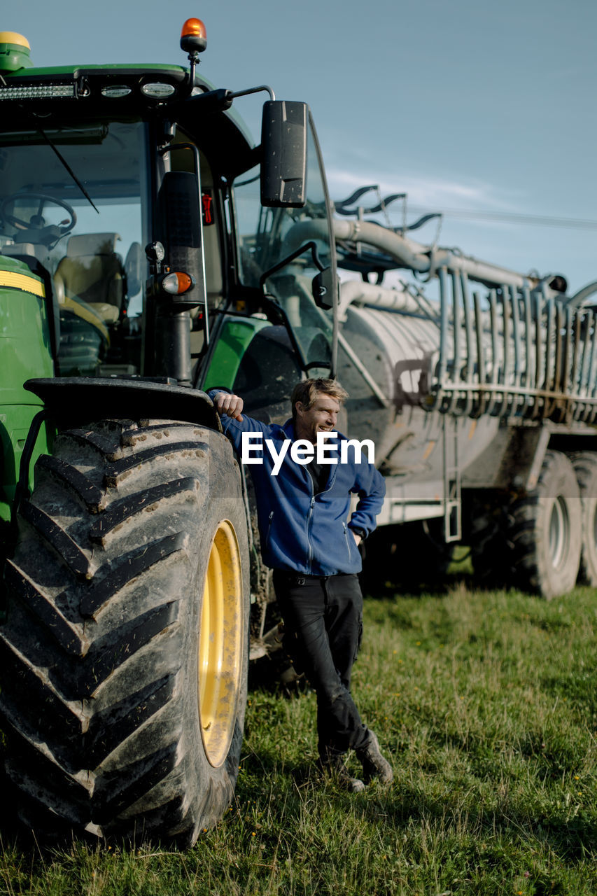 Happy mature farmer standing by tractor on field