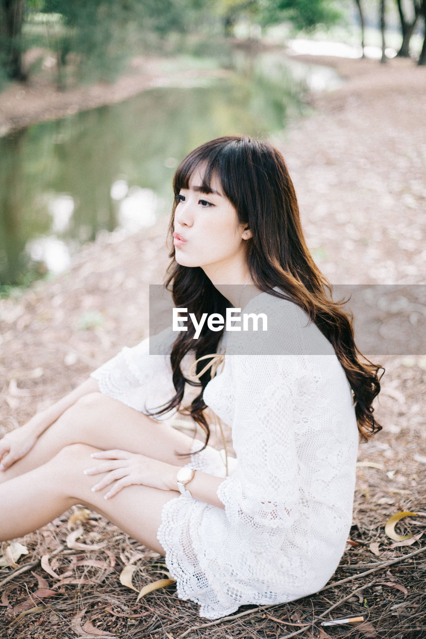 Side view of young woman looking away while sitting on field in forest