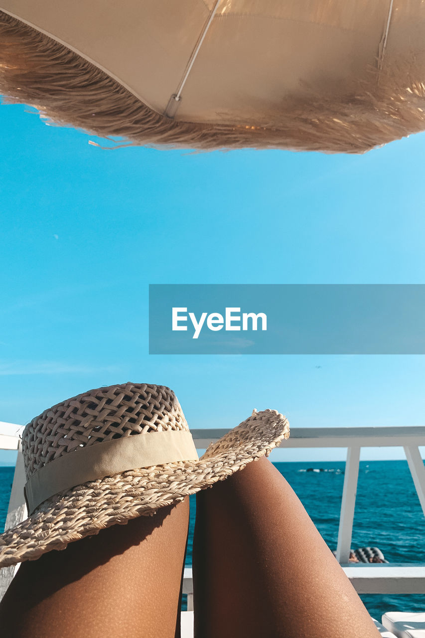 Midsection of woman with hat relaxing on yacht against sky