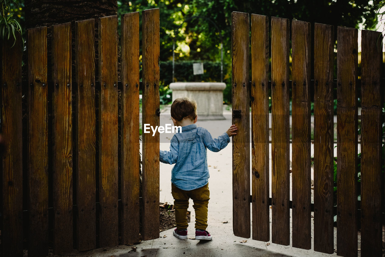 FULL LENGTH REAR VIEW OF BOY STANDING BY GATE