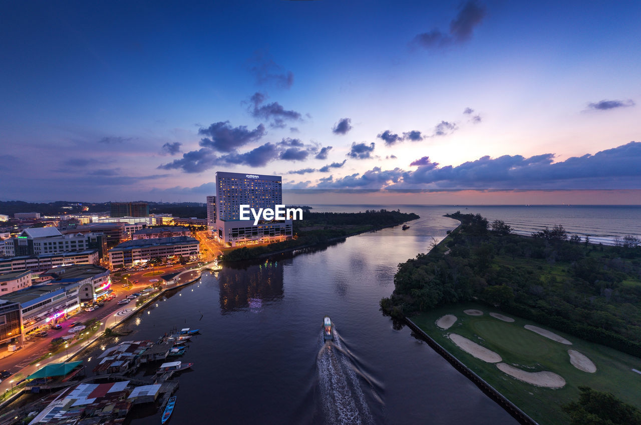 HIGH ANGLE VIEW OF ILLUMINATED CITY BY SEA AGAINST SKY