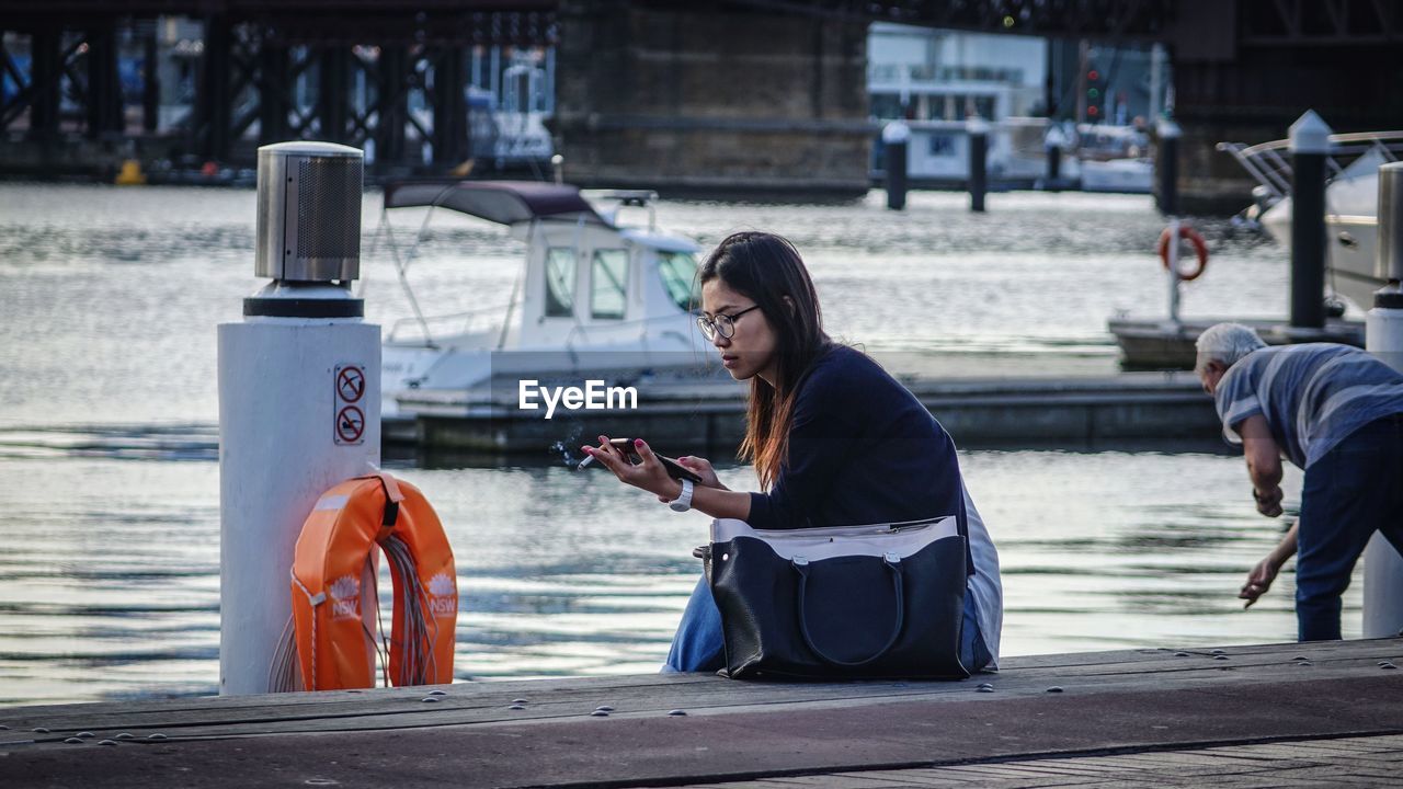 WOMAN USING MOBILE PHONE WHILE SITTING ON STREET AT PARK