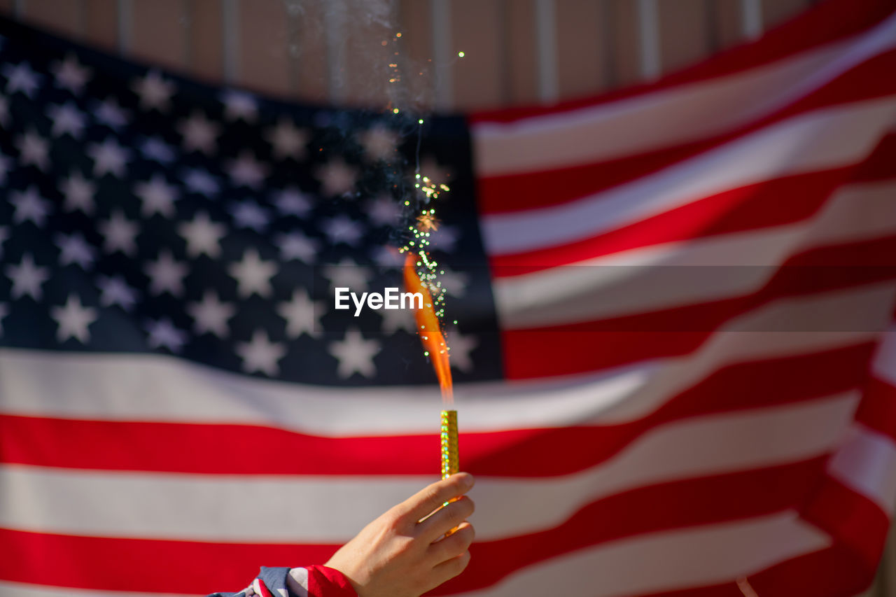 Close-up of hand holding firework against american flag