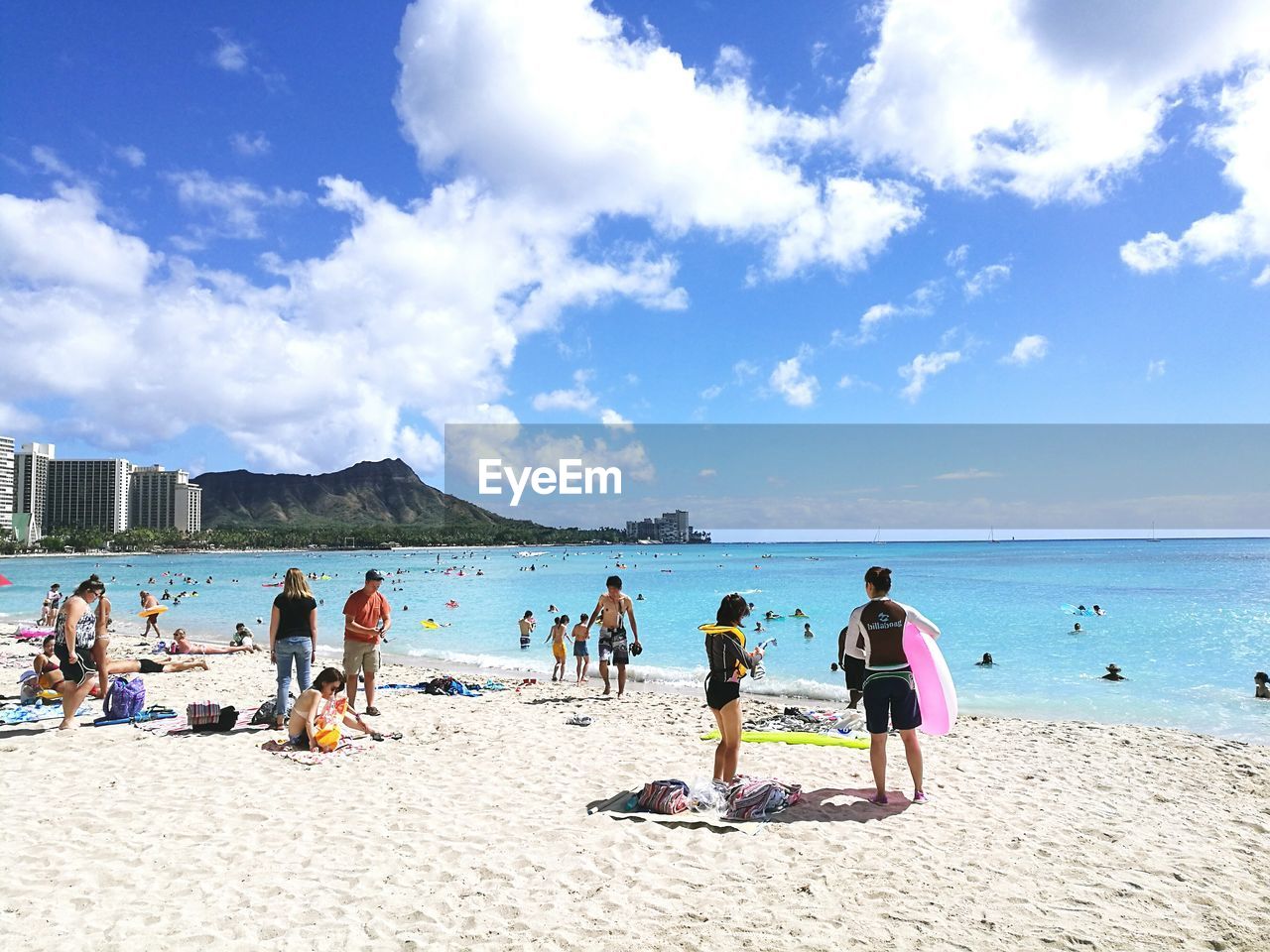 People at beach against cloudy sky during sunny day