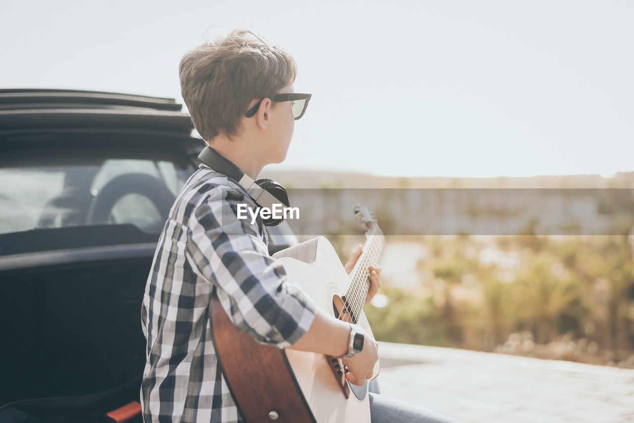 Young boy playing guitar and using smartphone outdoor. teen enjoying music