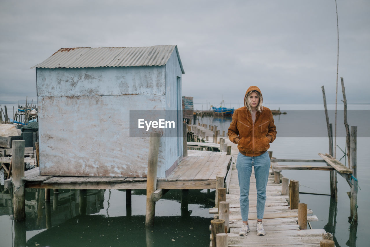 Portrait of young woman standing by river against sky