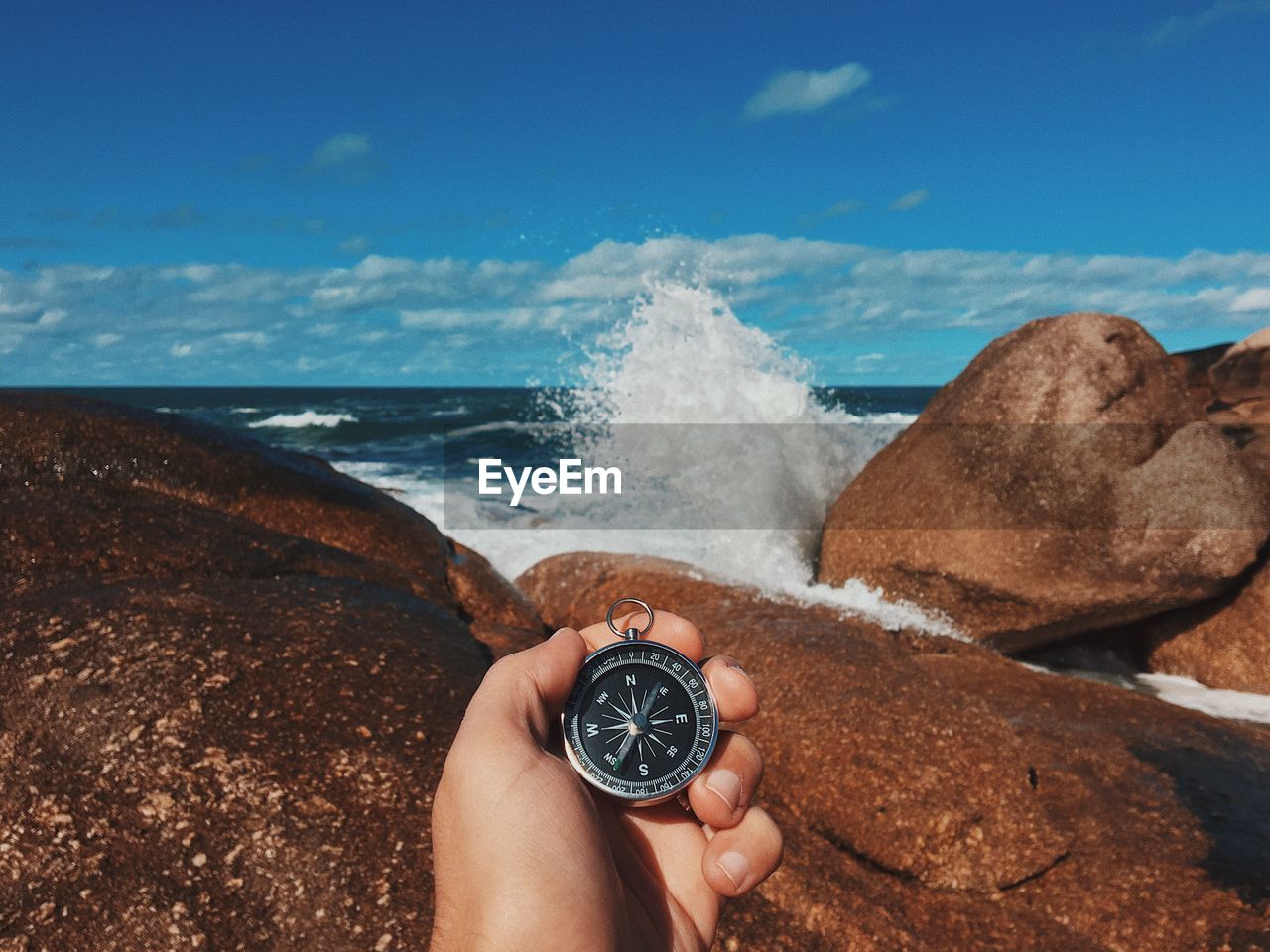 Cropped image of person holding navigational compass against rocky shore