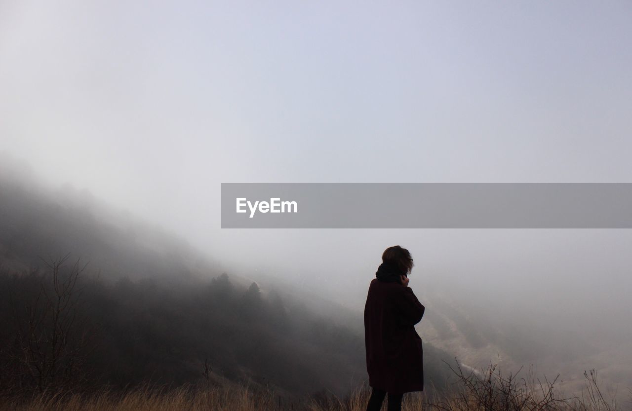 Rear view of woman standing on mountain in foggy weather