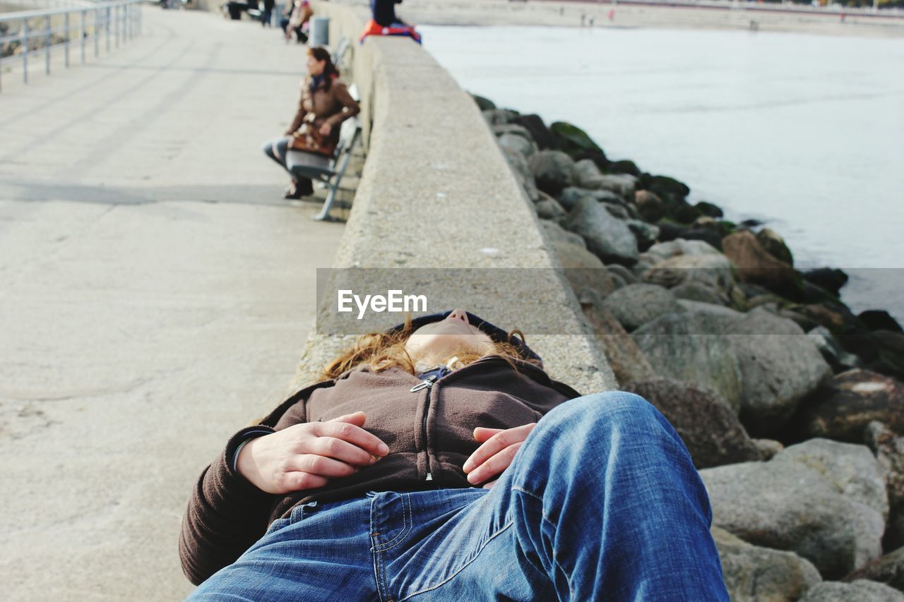 Woman lying on retaining wall by sea