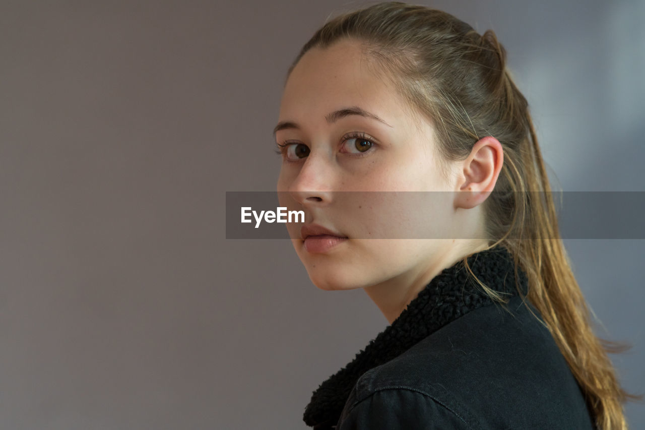 Close-up portrait of young woman against gray background