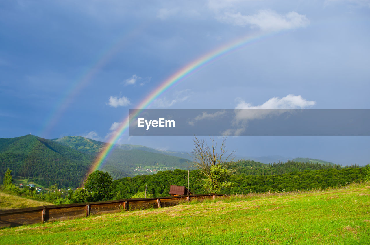 Scenic view of double rainbow over grassy field against sky