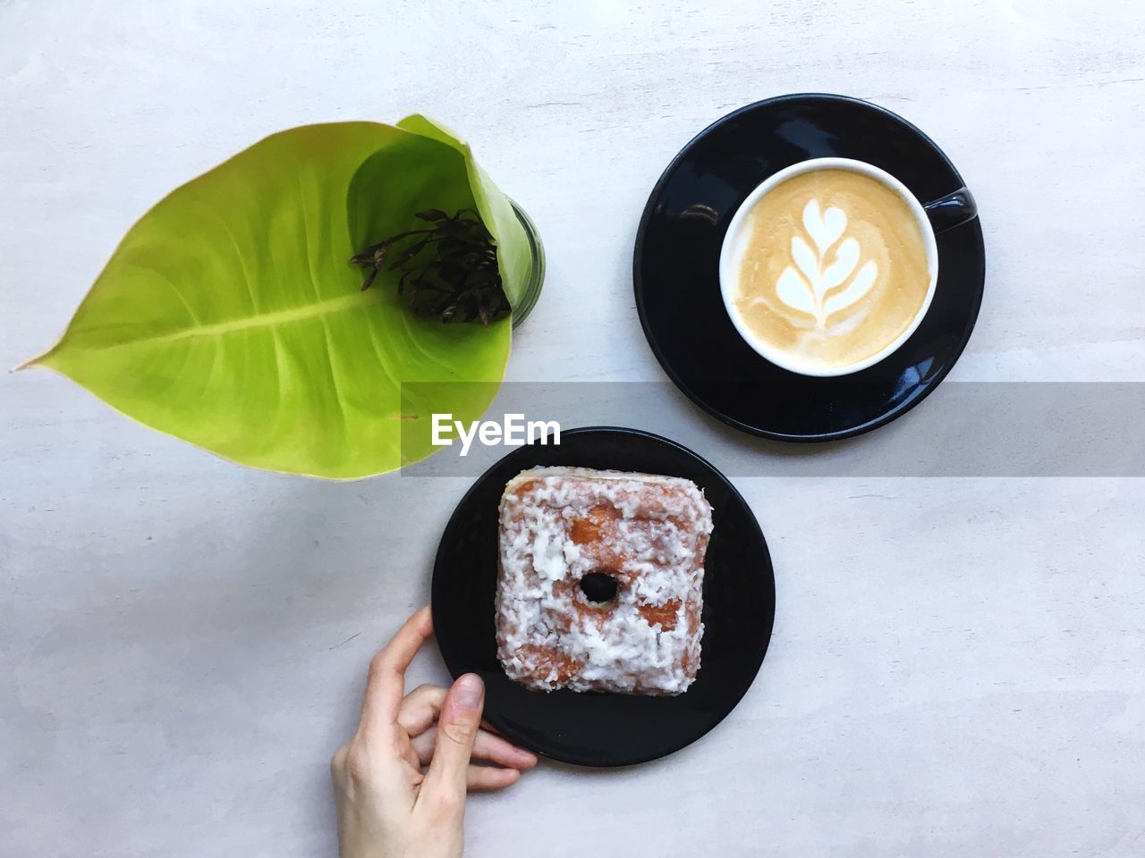 Cropped hand holding plate with donut by coffee cup on table