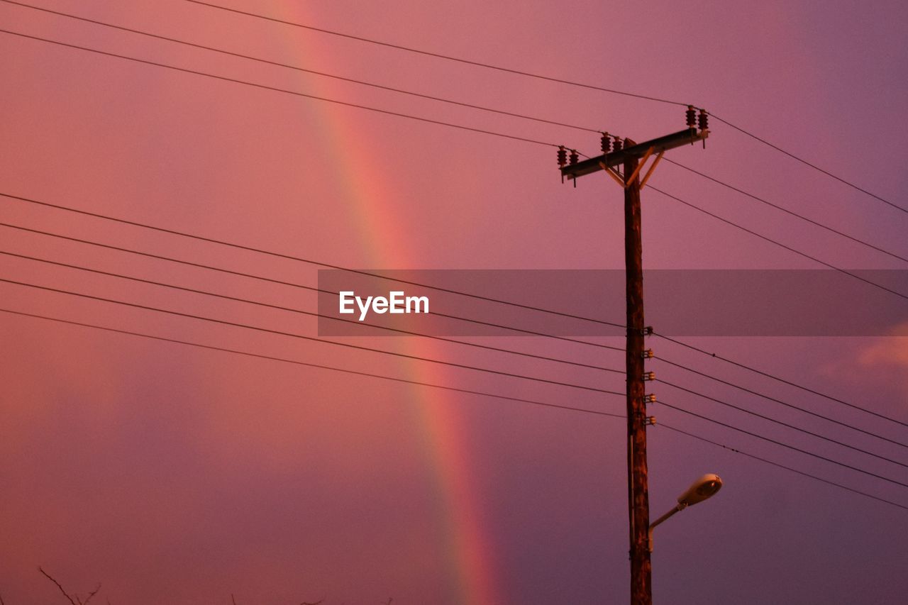 Low angle view of silhouette electricity pylon against sky and rainbow 