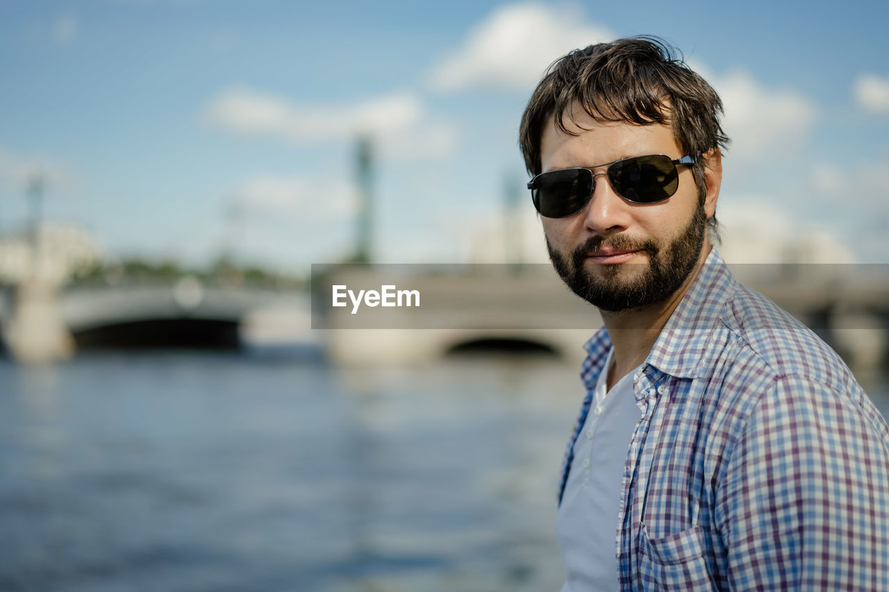 Handsome caucasian bearded man wearing sunglasses standing by the river neva, saint petersburg