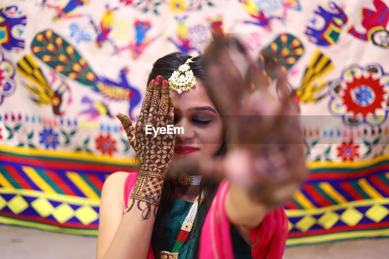 Close-up of bride with henna tattoo hiding face with hand