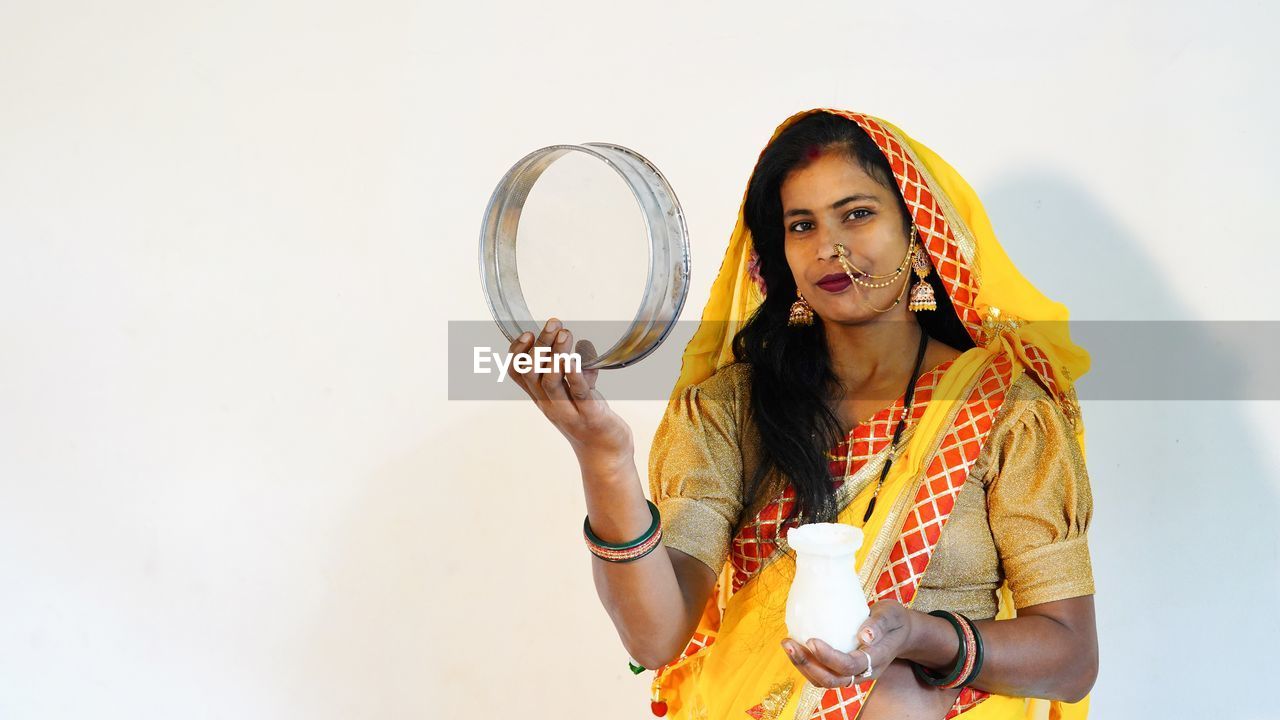 Portrait of young woman standing against white background. happy karva chauth festival