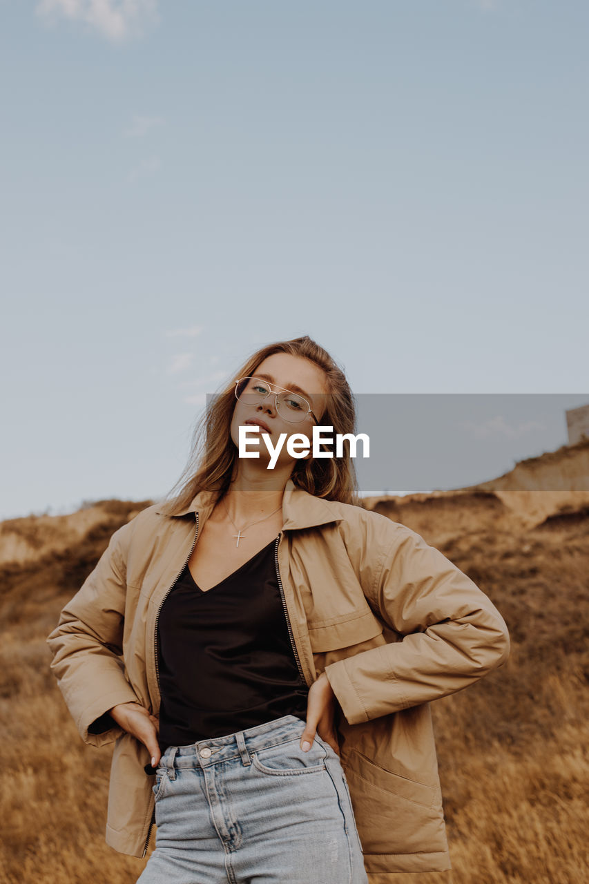 Portrait of young woman standing by plants against sky