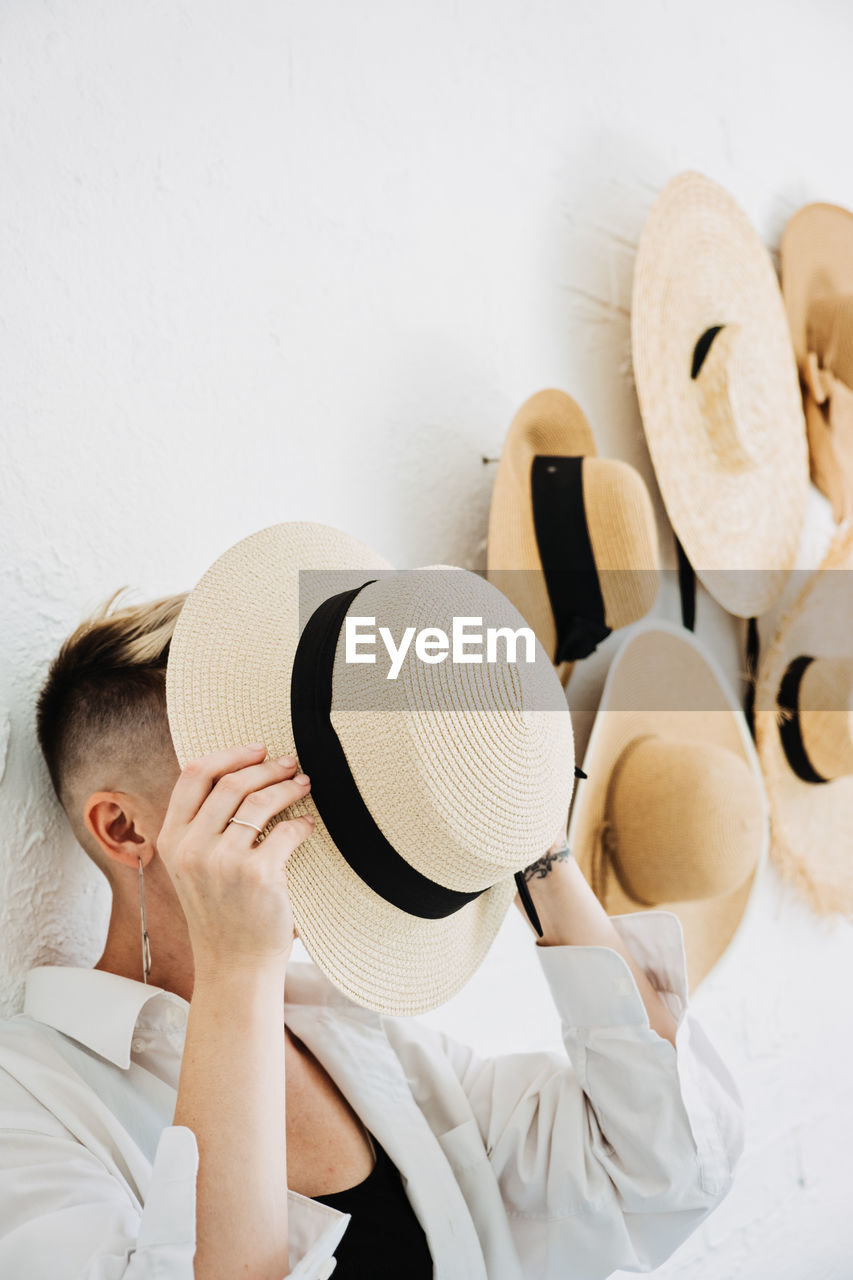 Hipster modern woman and many straw hats like interior decorate the walls in apartment