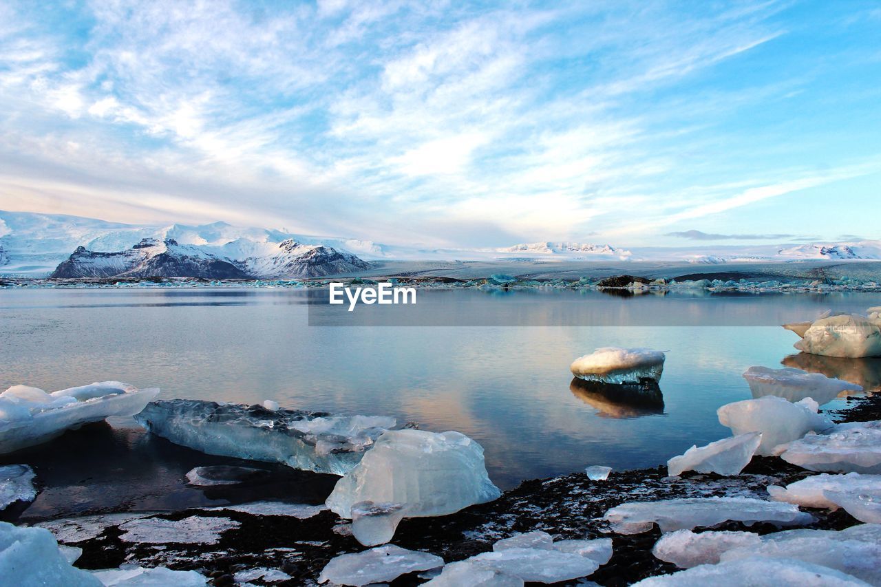 Scenic view of snowcapped mountains by lagoon against cloudy sky