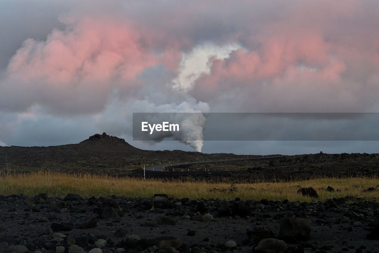 Smoke emitting from geothermal pool on landscape against sky