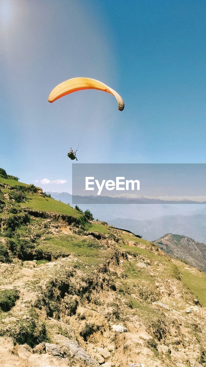 Person paragliding over mountain against sky