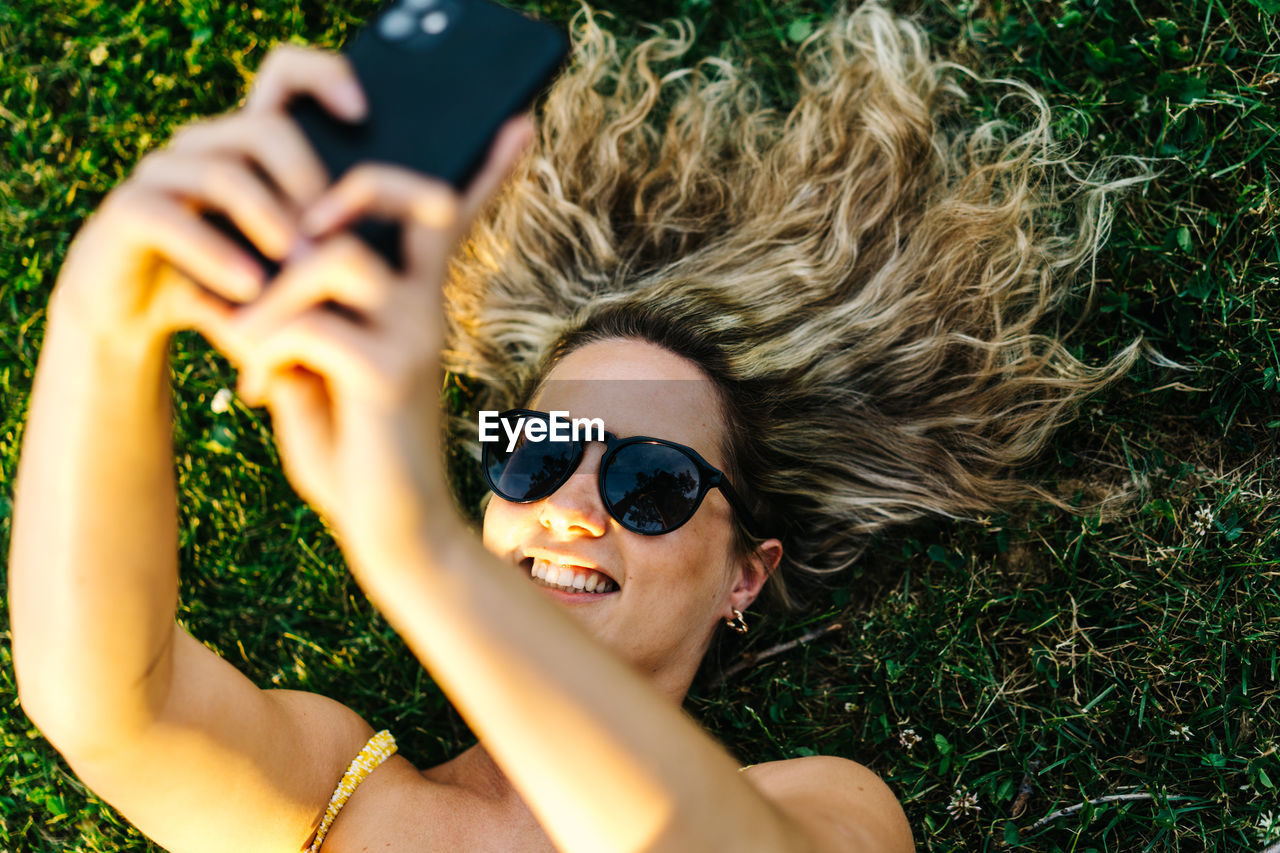 HIGH ANGLE VIEW OF WOMAN WEARING SUNGLASSES LYING ON FIELD