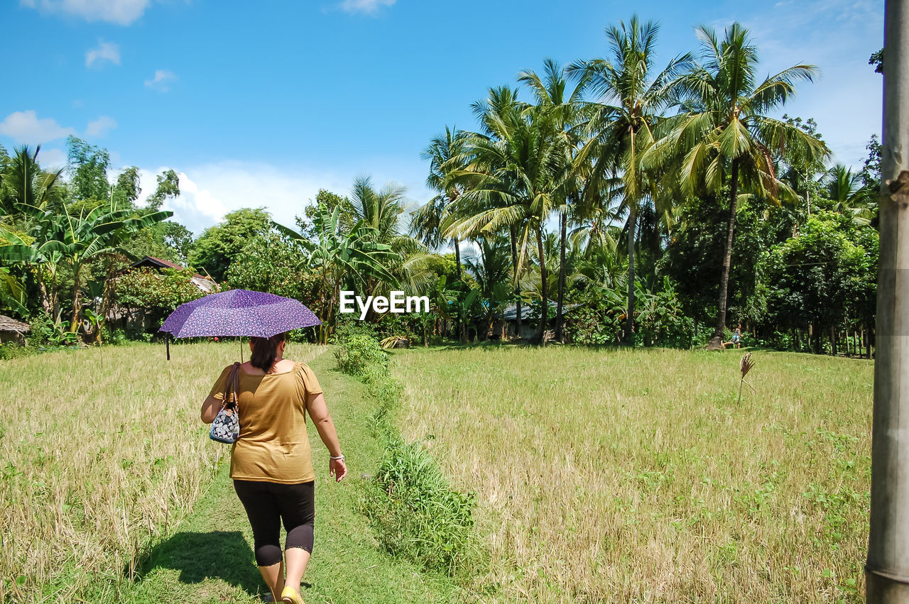 Rear view of woman walking on field against sky