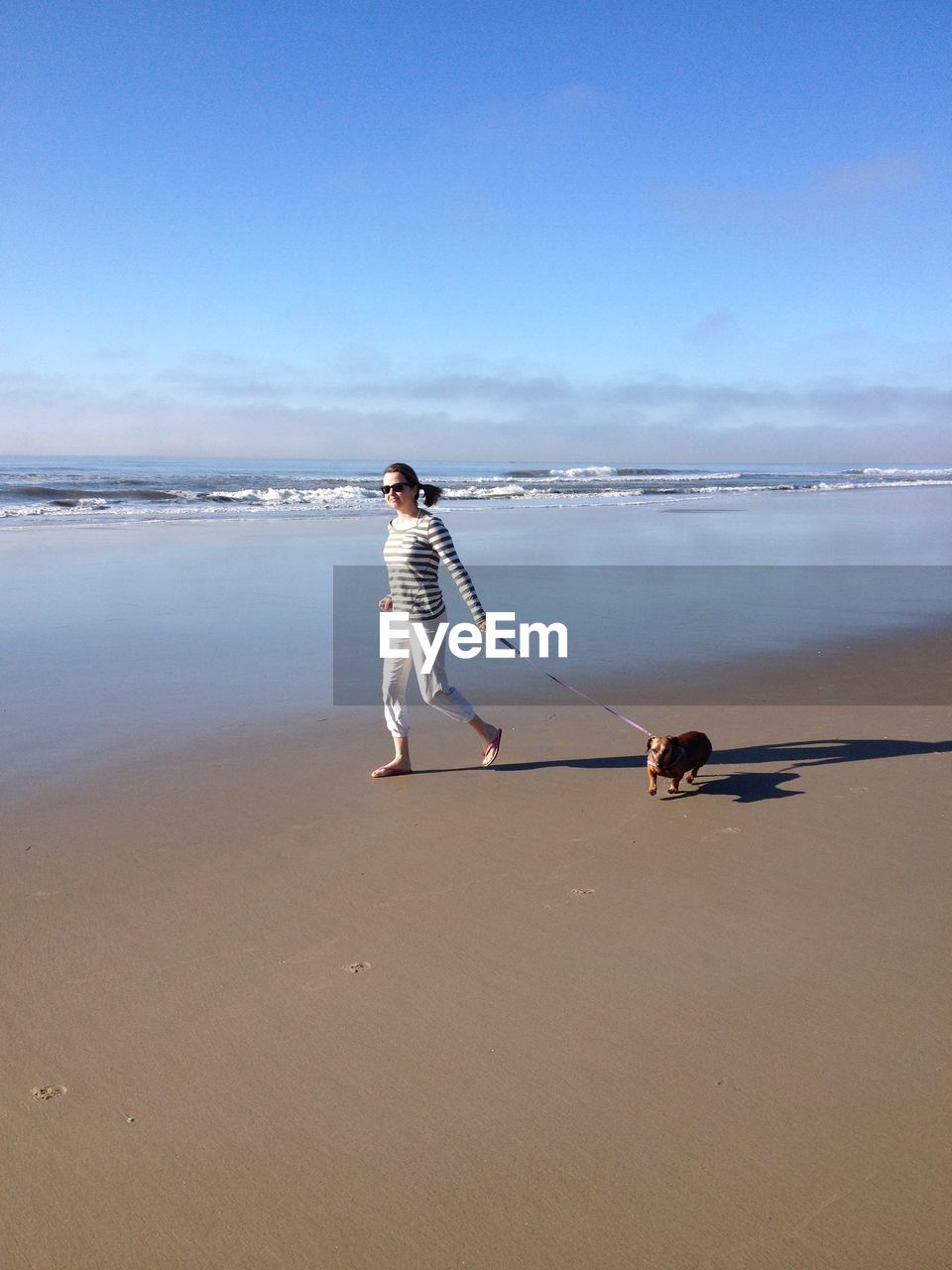 Woman walking with dog on sand against sea at beach