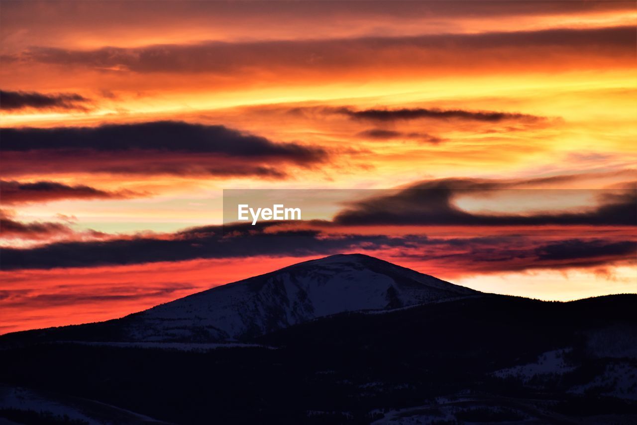 SCENIC VIEW OF DRAMATIC SKY OVER SILHOUETTE MOUNTAINS DURING SUNSET