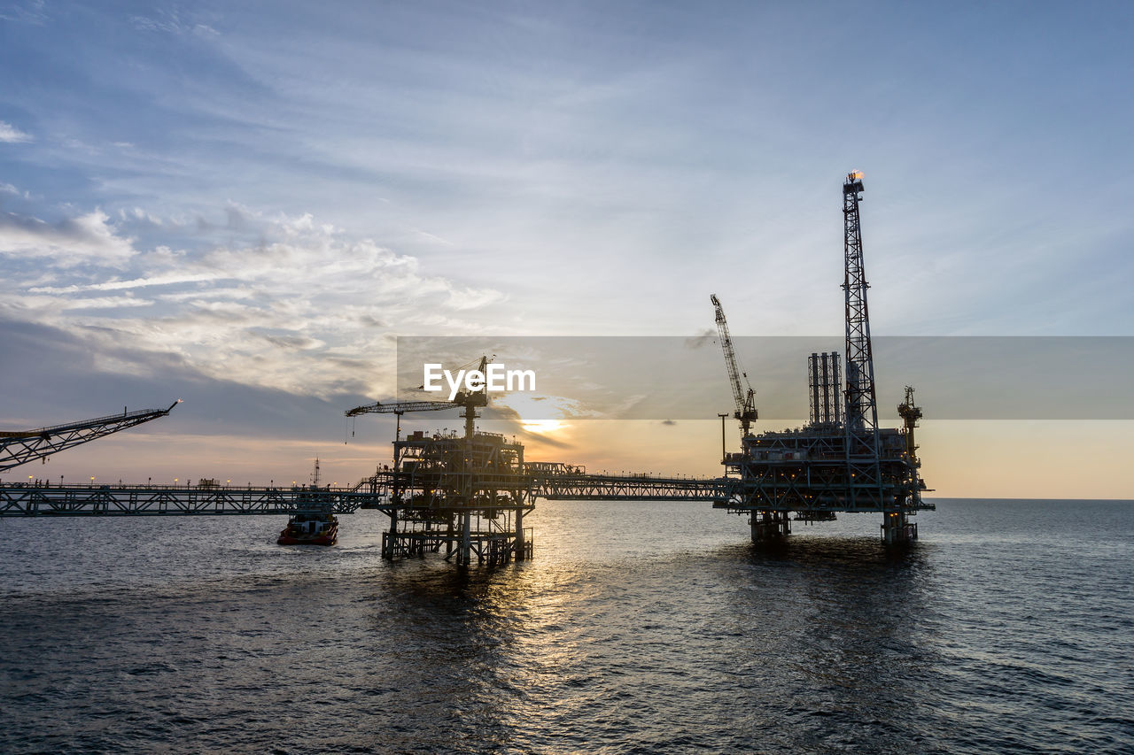 CRANES AT COMMERCIAL DOCK AGAINST SKY AT SUNSET