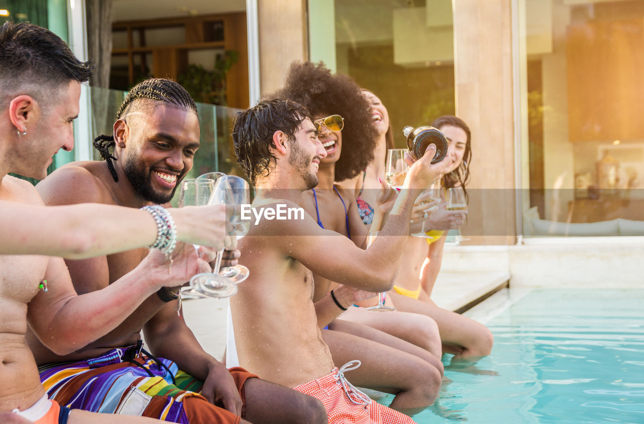 Friends enjoying drinks while sitting at poolside